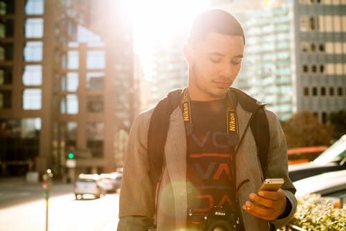 A black man texting on a brightly lit street
