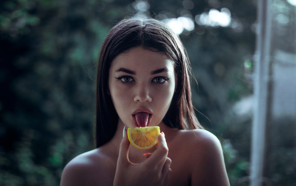 A beautiful woman licking an orange slice