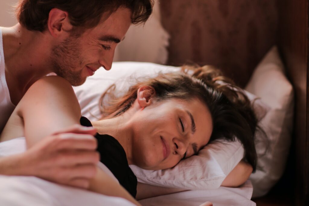 A man in bed next to an attractive woman. He is waking her up. 