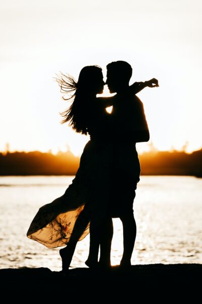 The silihouette of a man and woman together romantically near a lake at sunset 