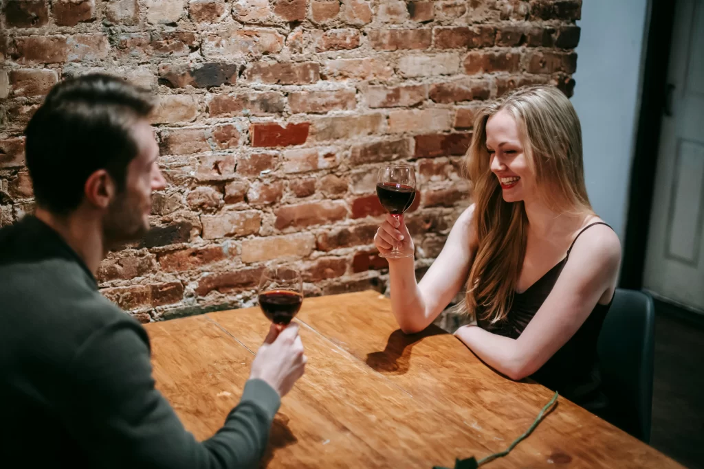 Man and woman drinking wine from glasses at a wooden table on a date