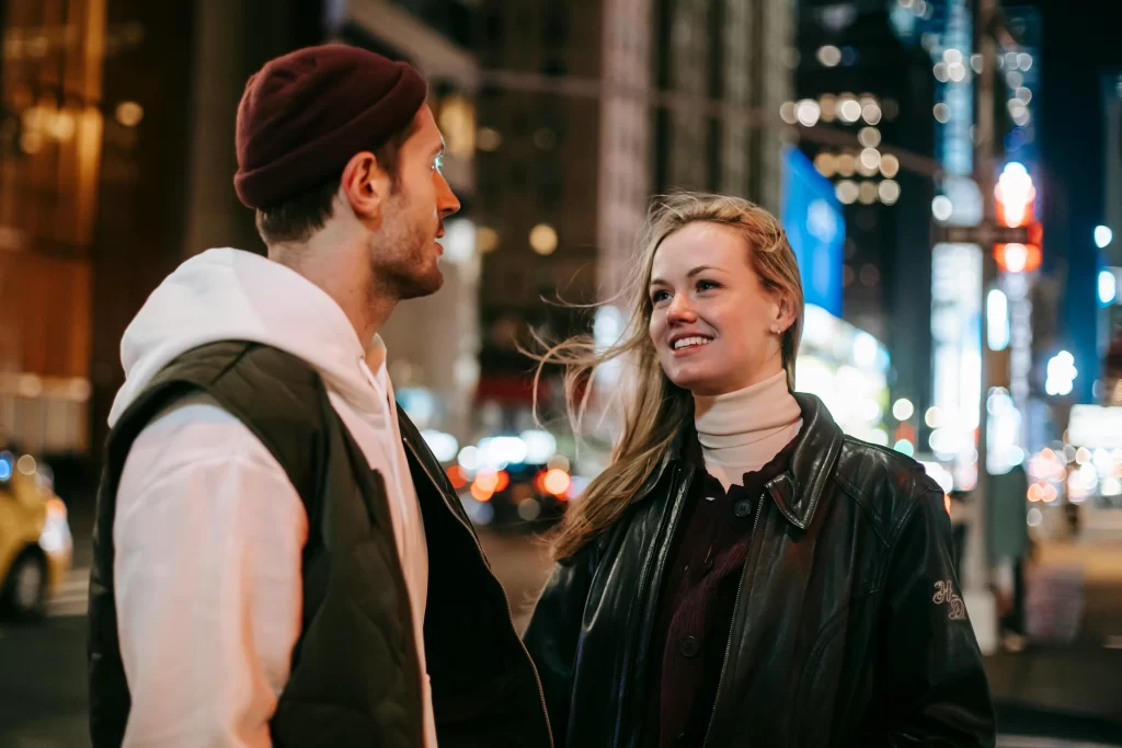 A man talking to a pretty women on the street in a city at night